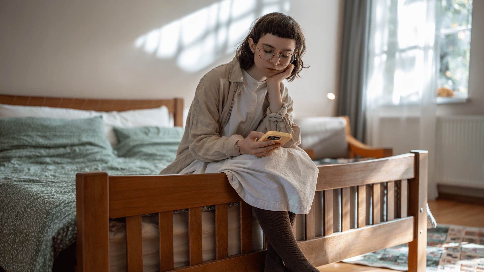 woman sitting down on bed and looking at phone