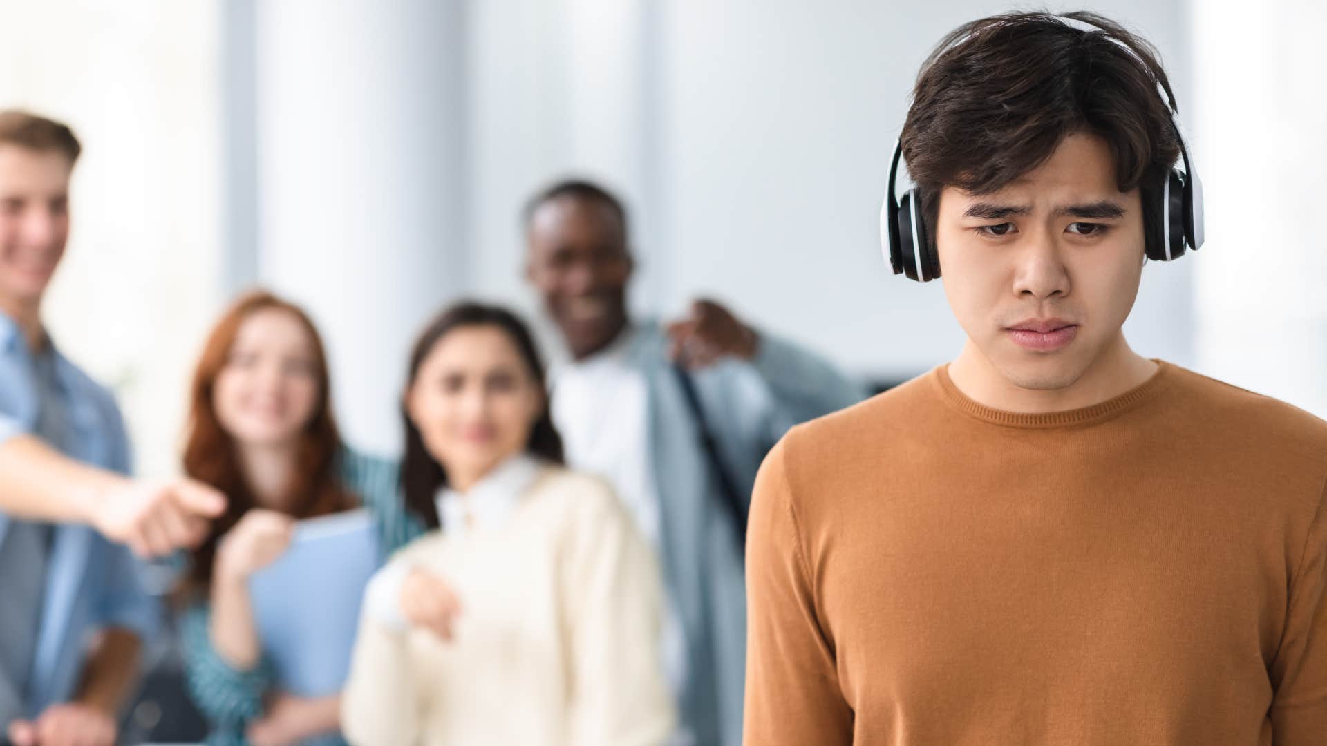 sad man wearing headphones standing away from group of people