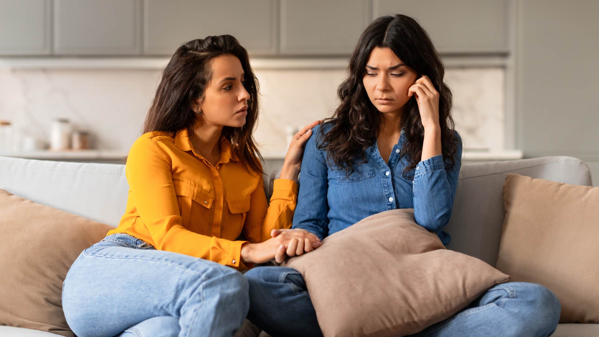  young woman comforting depressed friend holding her hand on couch