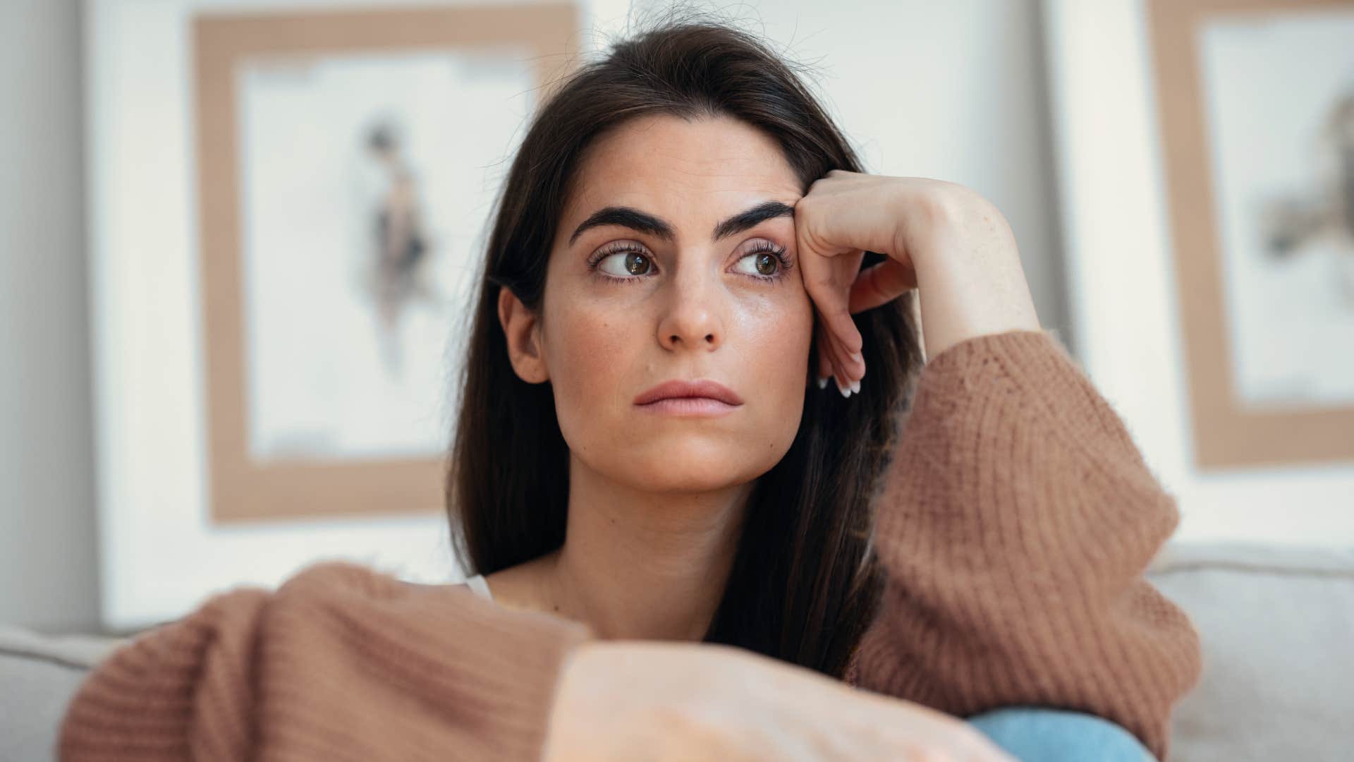 Shot of young woman overthinking while sitting on the couch at home