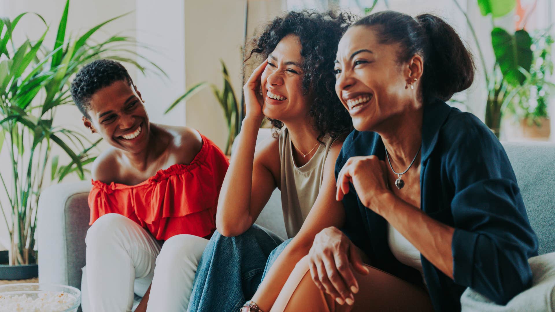 Three women smiling and laughing together on a couch.