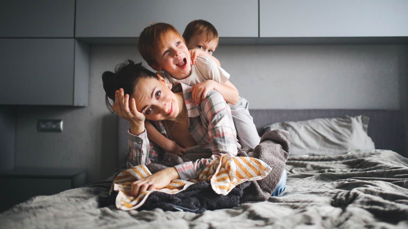 tired mother on bed with kids climbing on her back