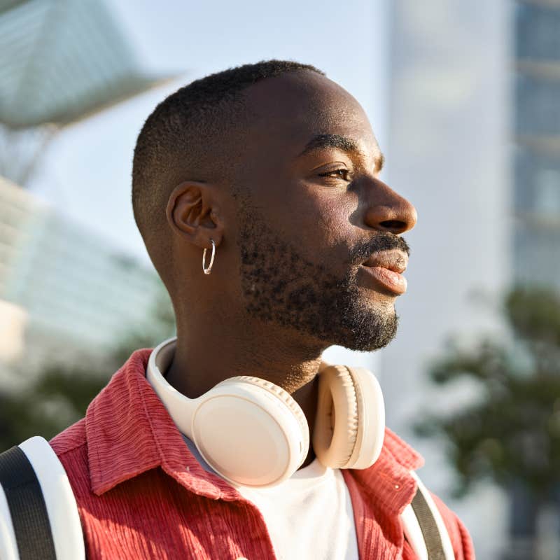 Portrait of young adult man standing on city street outdoors looking away