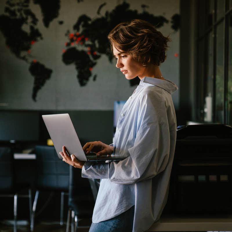 concentrated business woman wearing shirt using laptop while standing in modern workspace