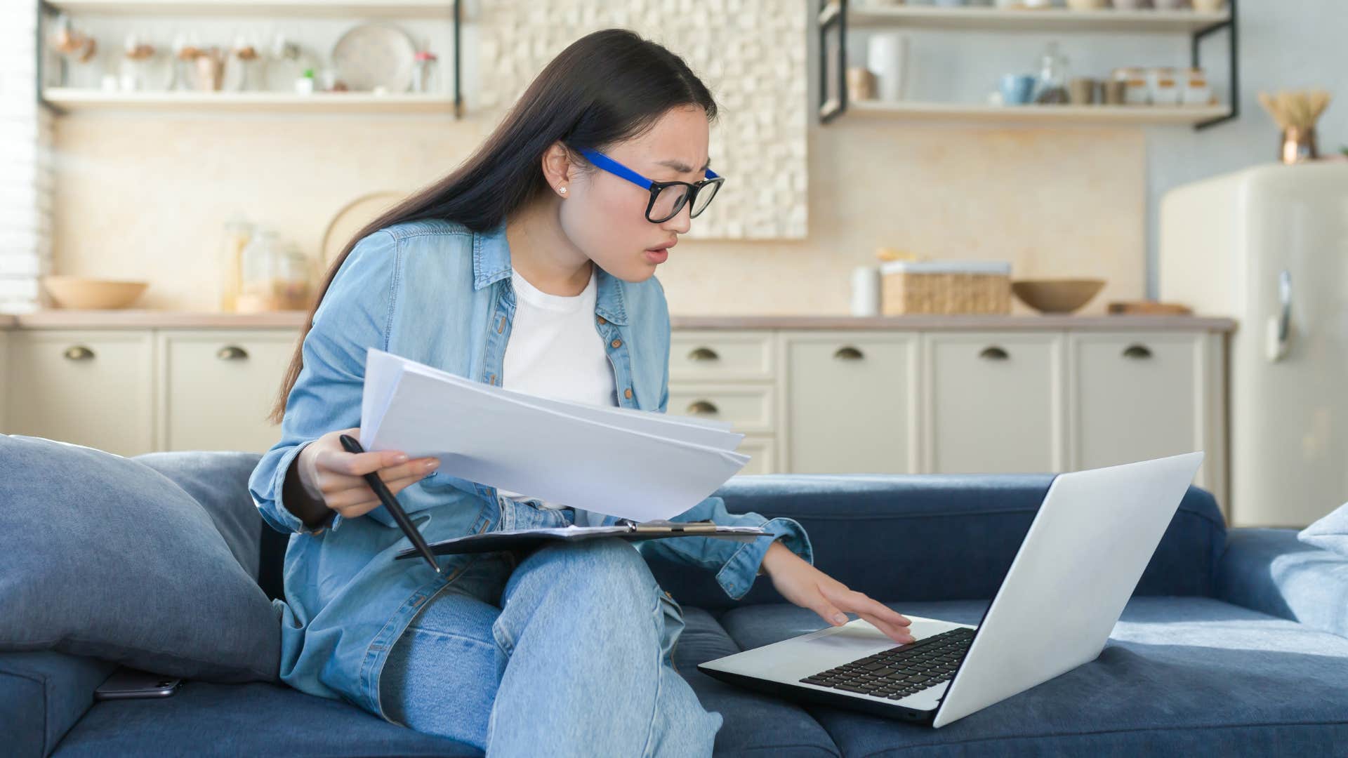 Woman looking stressed on her laptop sitting on the couch.