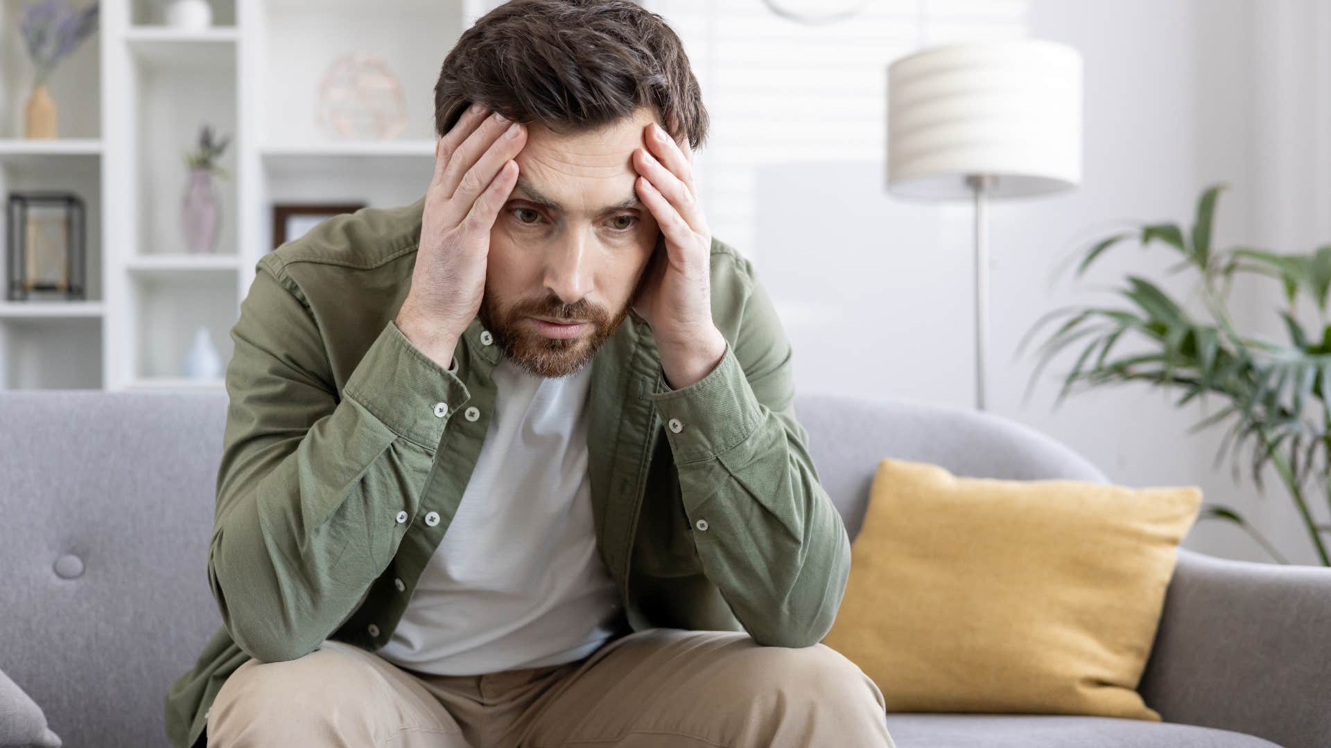 Man contemplating and holding his head on the couch.