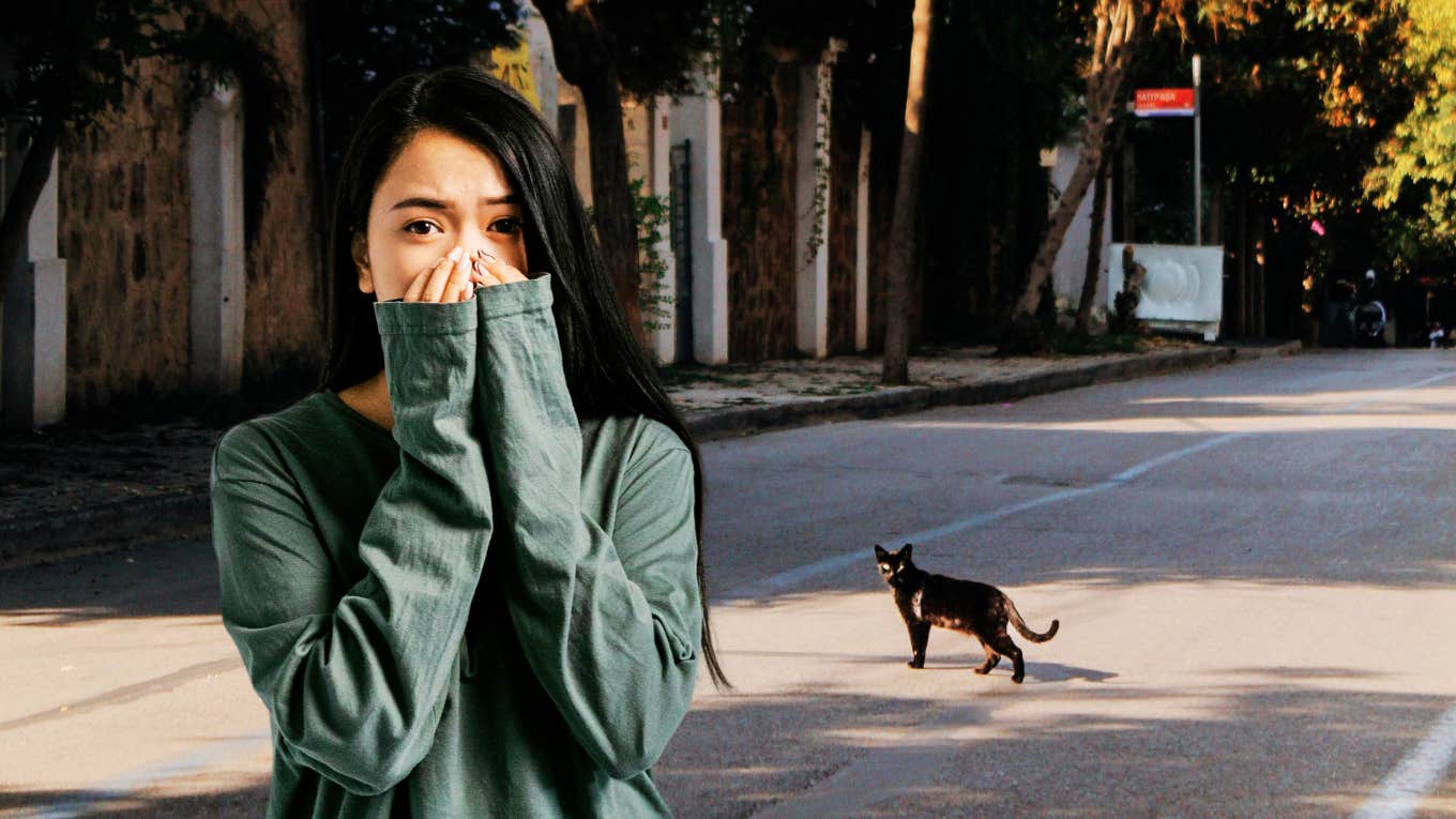 Worried superstitious woman, watching black cat cross her. 