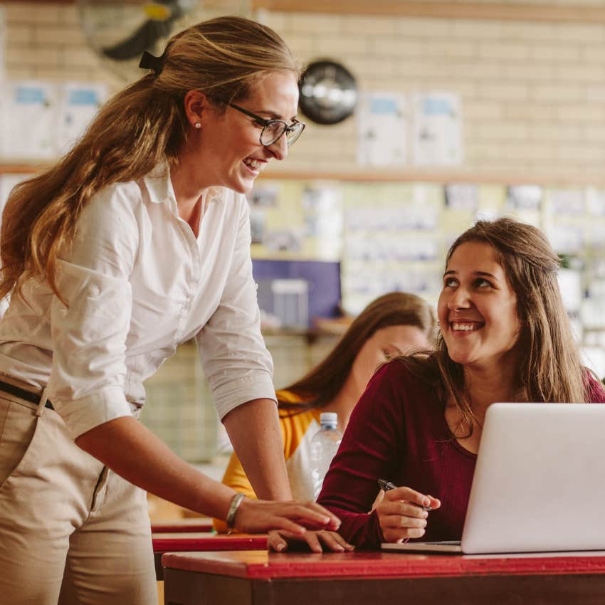 Teacher helping a high school student at her desk. 