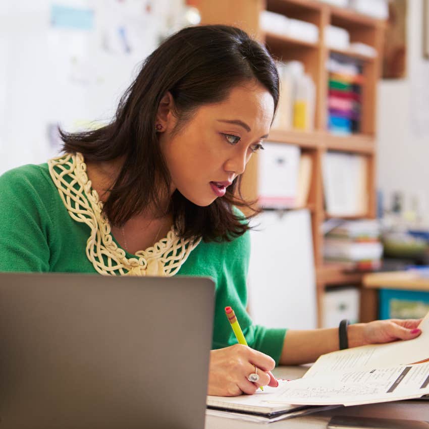 Teacher looking stressed grading homework at her desk. 