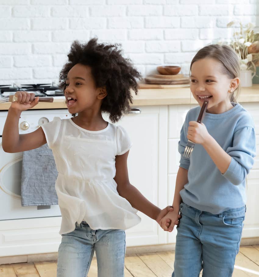 Two children hold hands and sing in kithcen