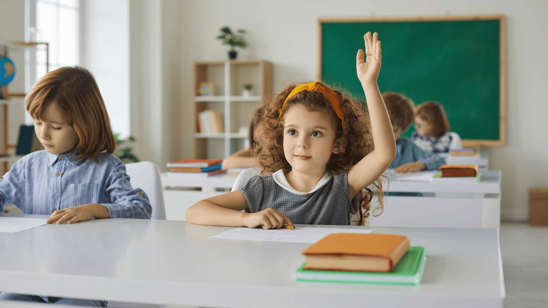 young girl raising her hand in class that doesn't have paper attendance register