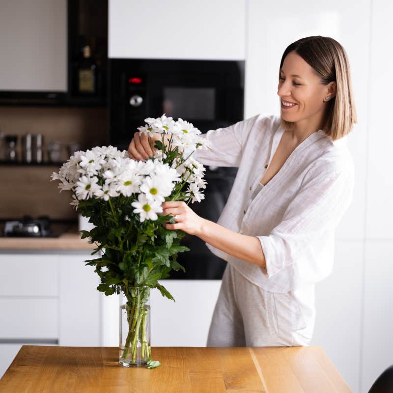 Happy and joyful young woman in white arranging white flowers at home in the kitchen