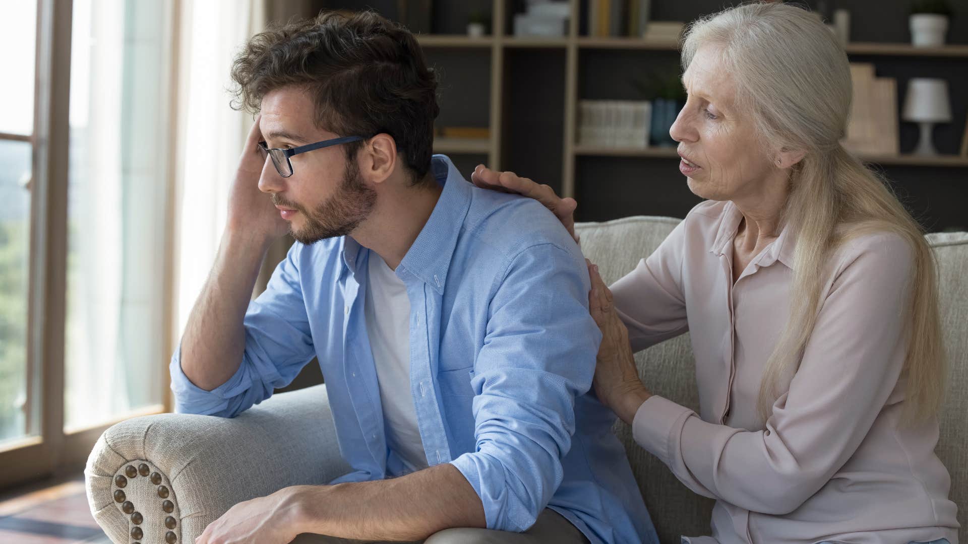 Older woman comforting her adult son at home.