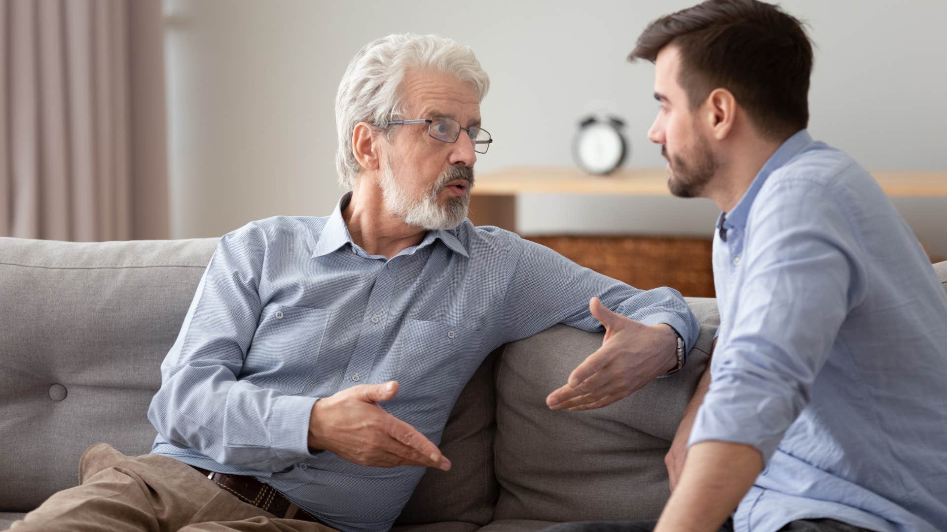 Older man talking to his adult son on the couch.