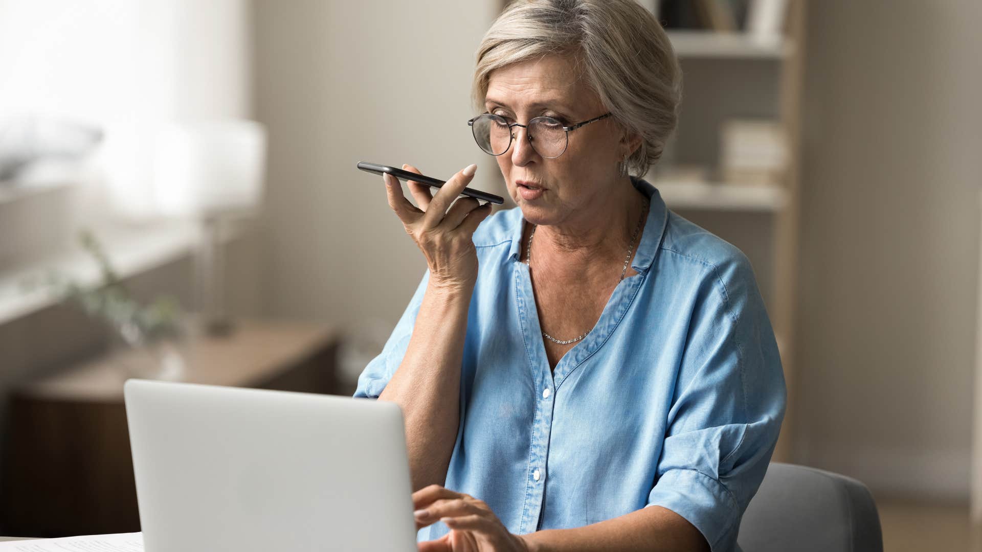 Older woman talking on the phone and typing on her laptop.