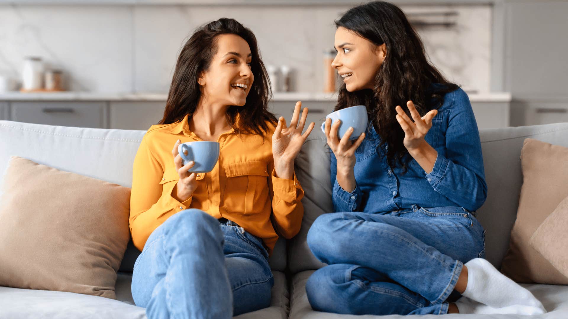 two women drinking hot drink and sitting on couch