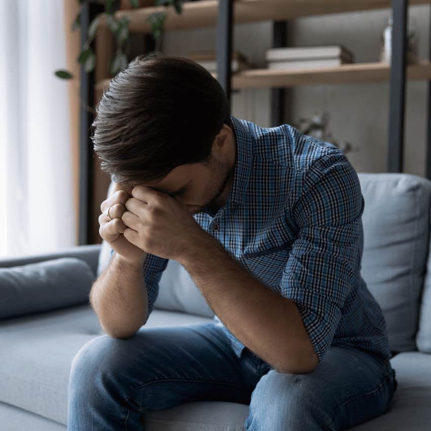 upset man with his head in his hands sitting on a couch alone