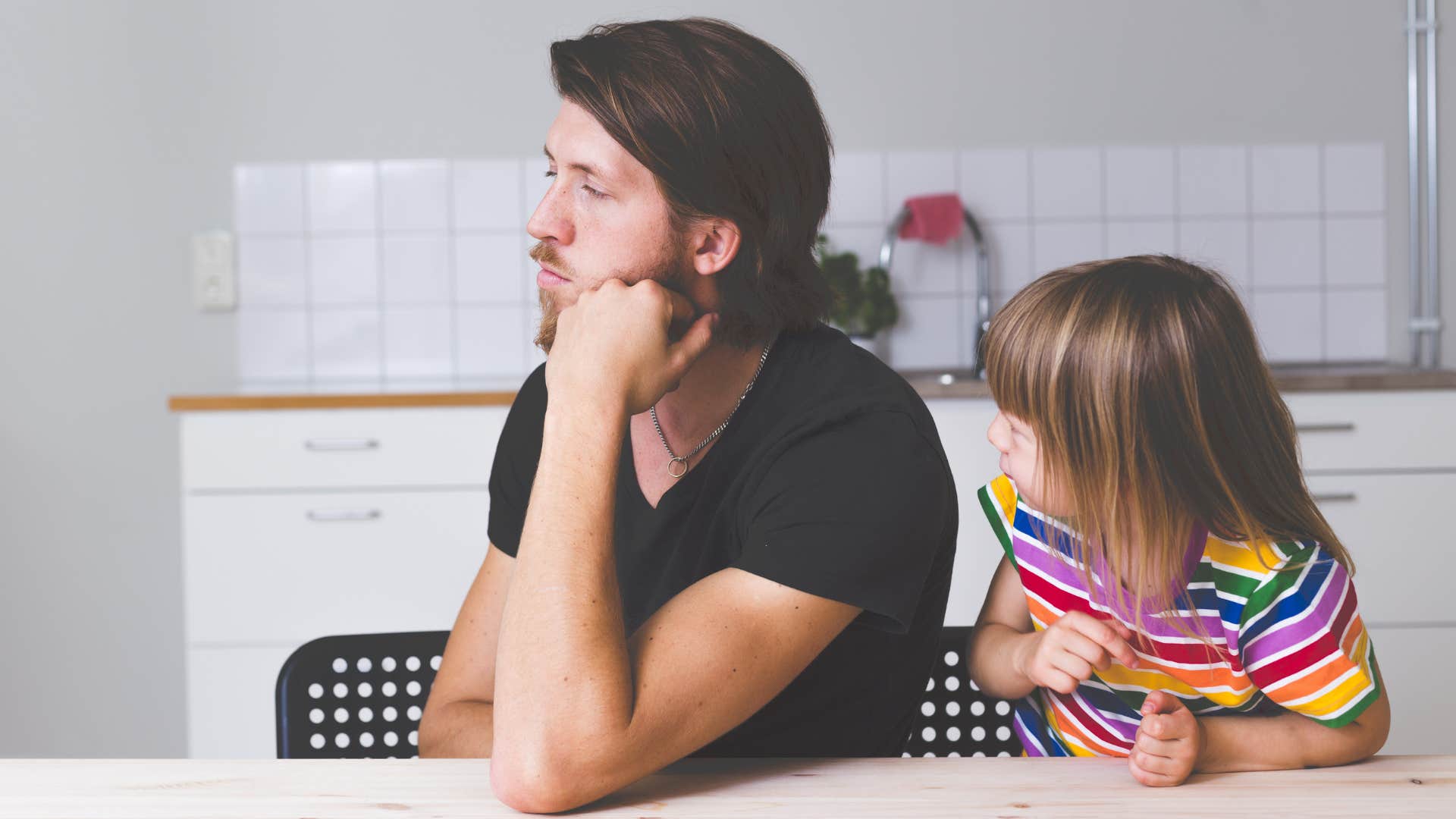 Dad ignoring his young daughter in the kitchen. 