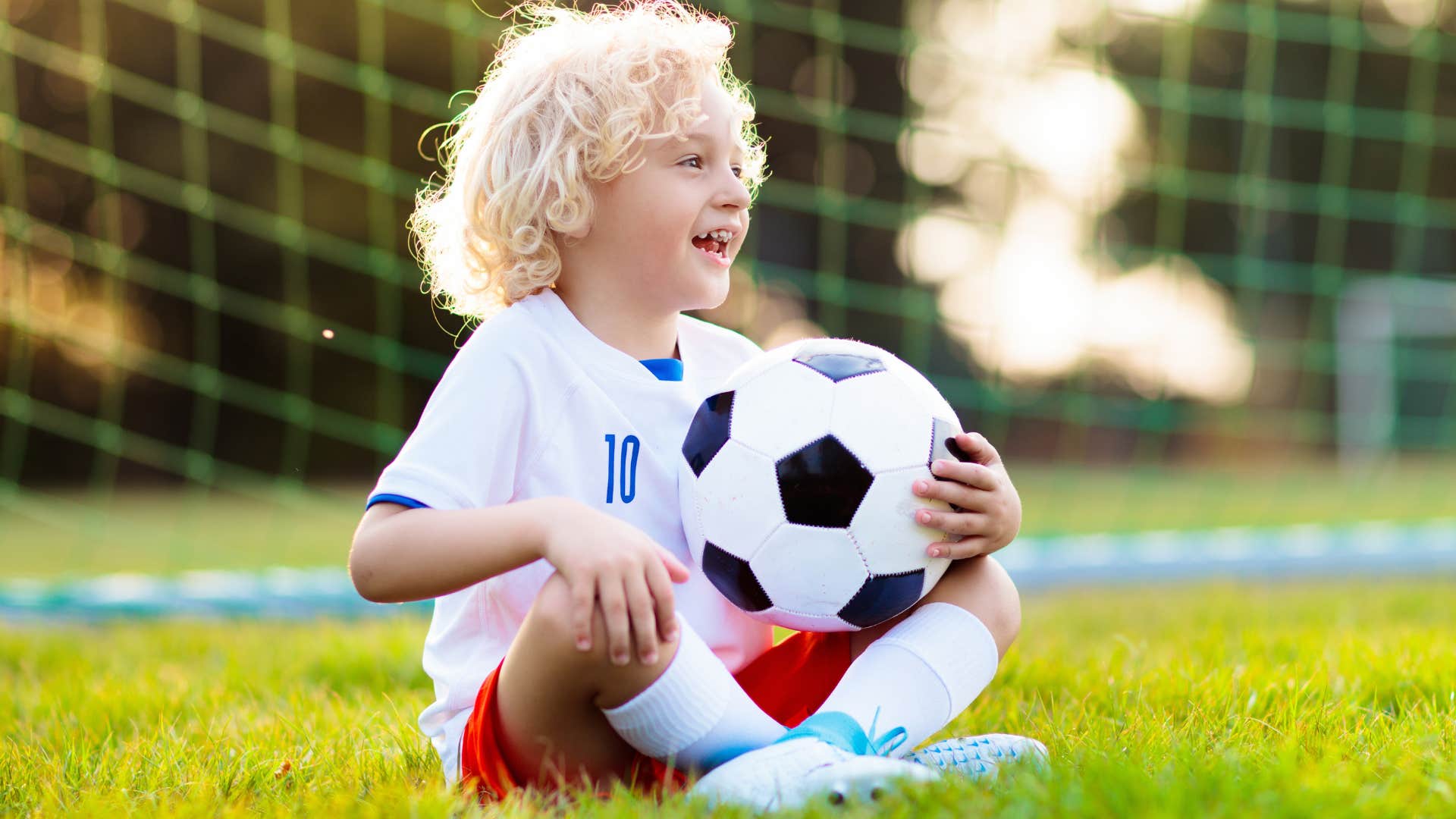 Little boy smiling while holding a soccer ball on a field. 