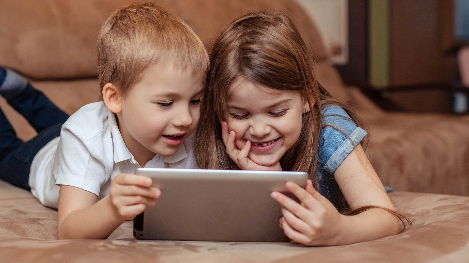 Kids smiling while typing on a tablet.