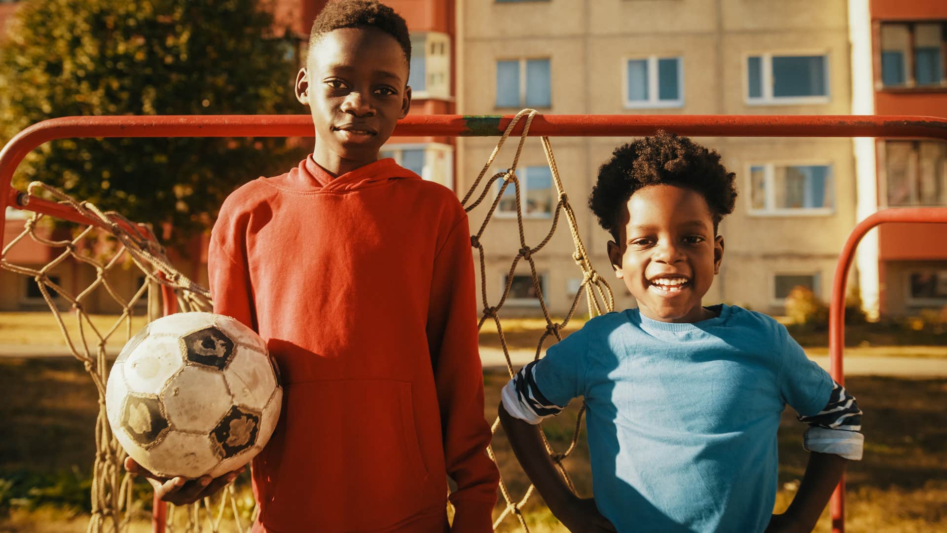 Two young siblings holding a soccer ball on a playground.