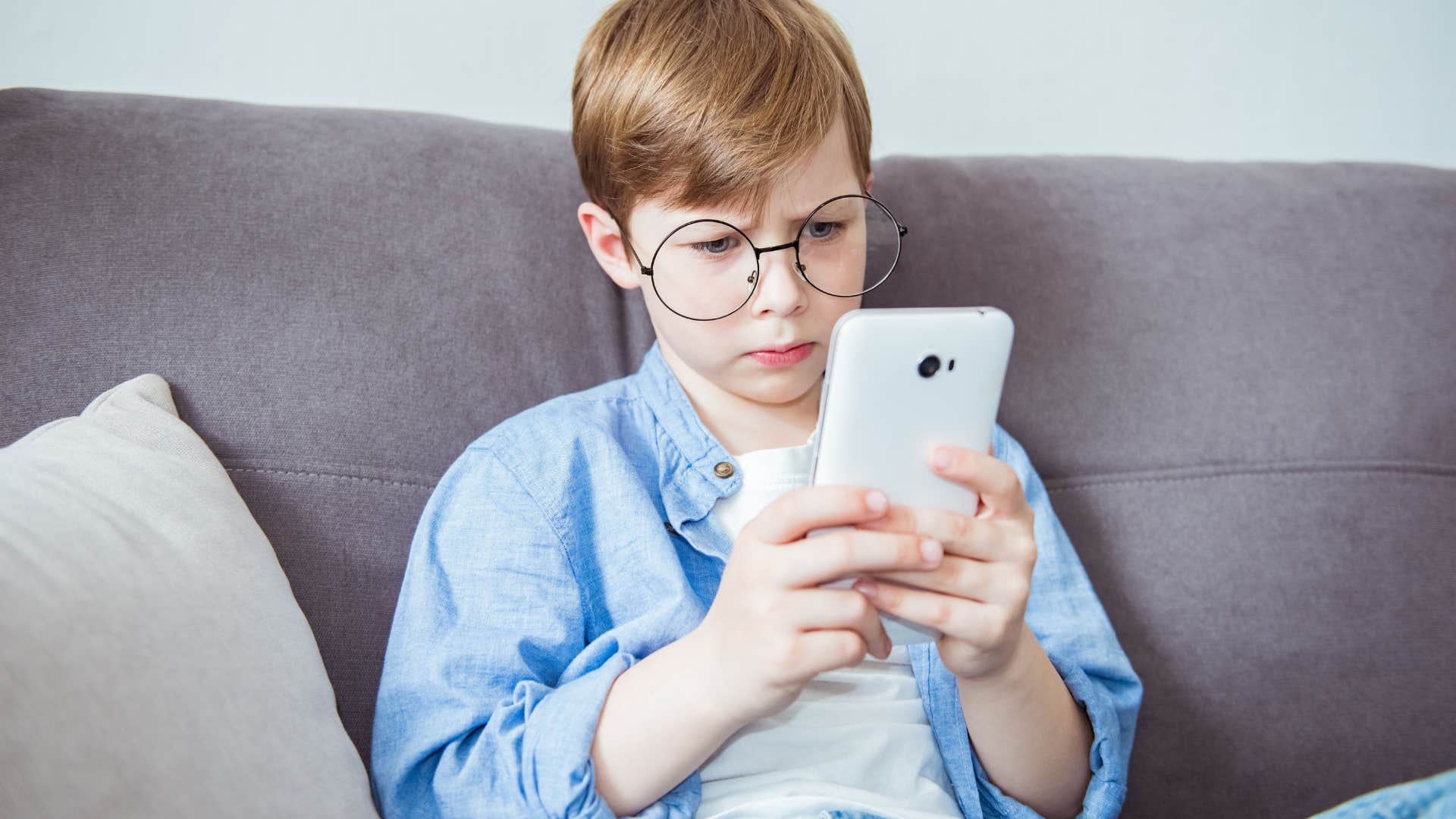 Young boy looking upset while typing on his phone.