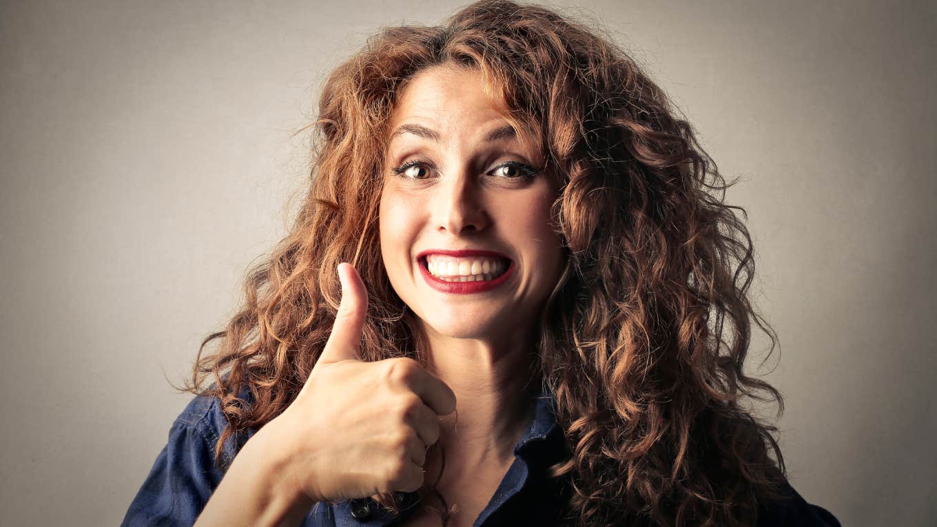 Woman with curly red hair giving an enthusiastic thumbs up