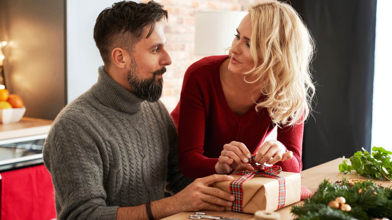 married couple wrapping holiday gifts together so wife isn't doing al the work