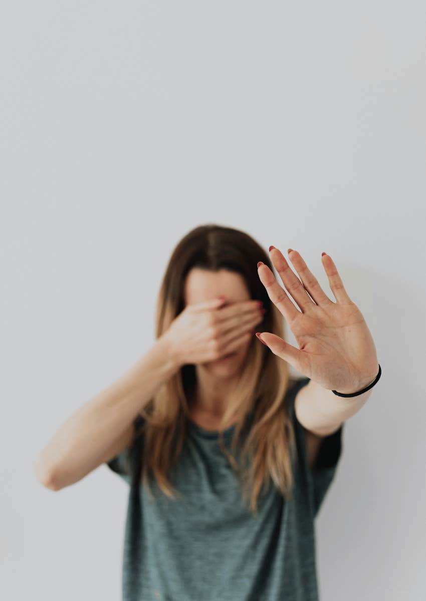 woman covering her face and holding her hand up