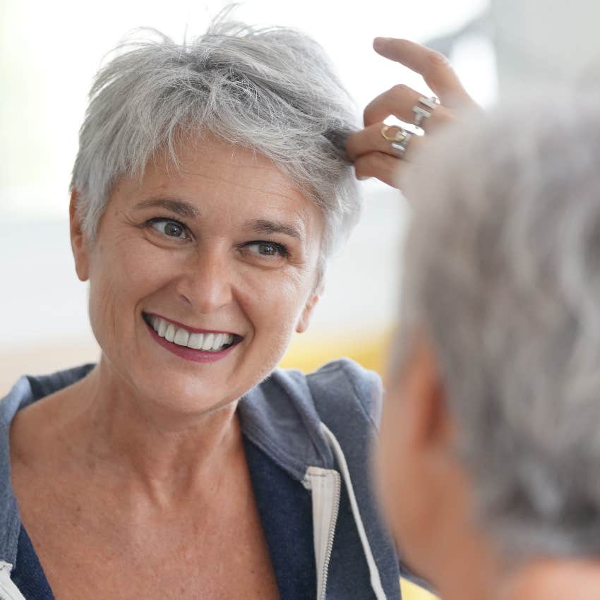 Happy older woman looking at hair in mirror