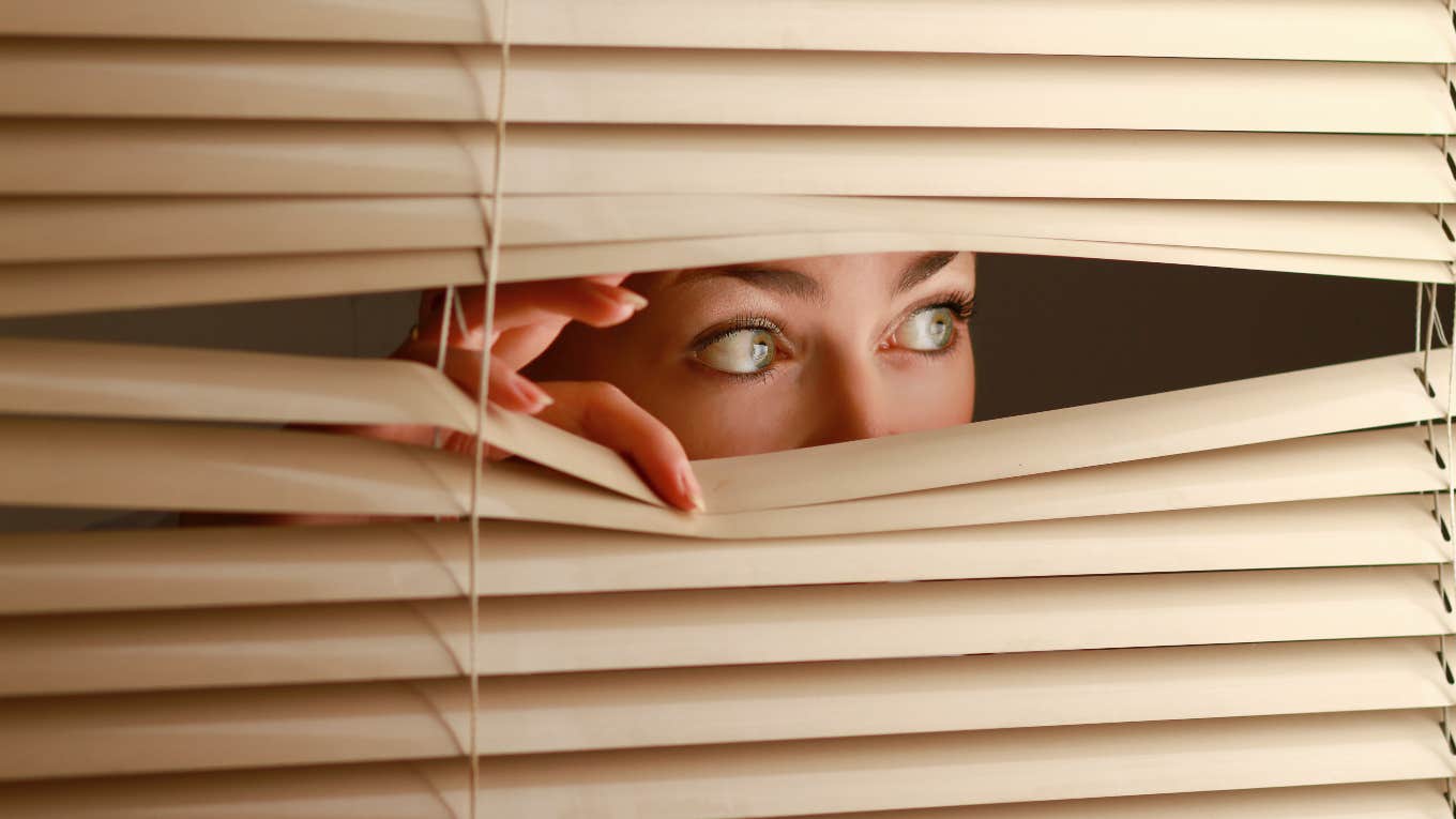 woman looking out the blinds of haunted house at rug buried in backyard