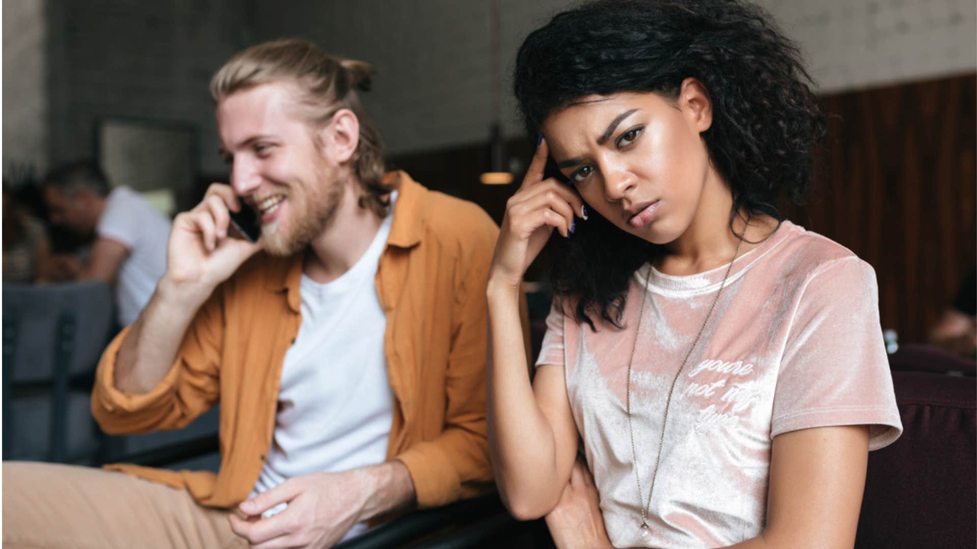 Woman looking upset while her boyfriend talks on the phone. 