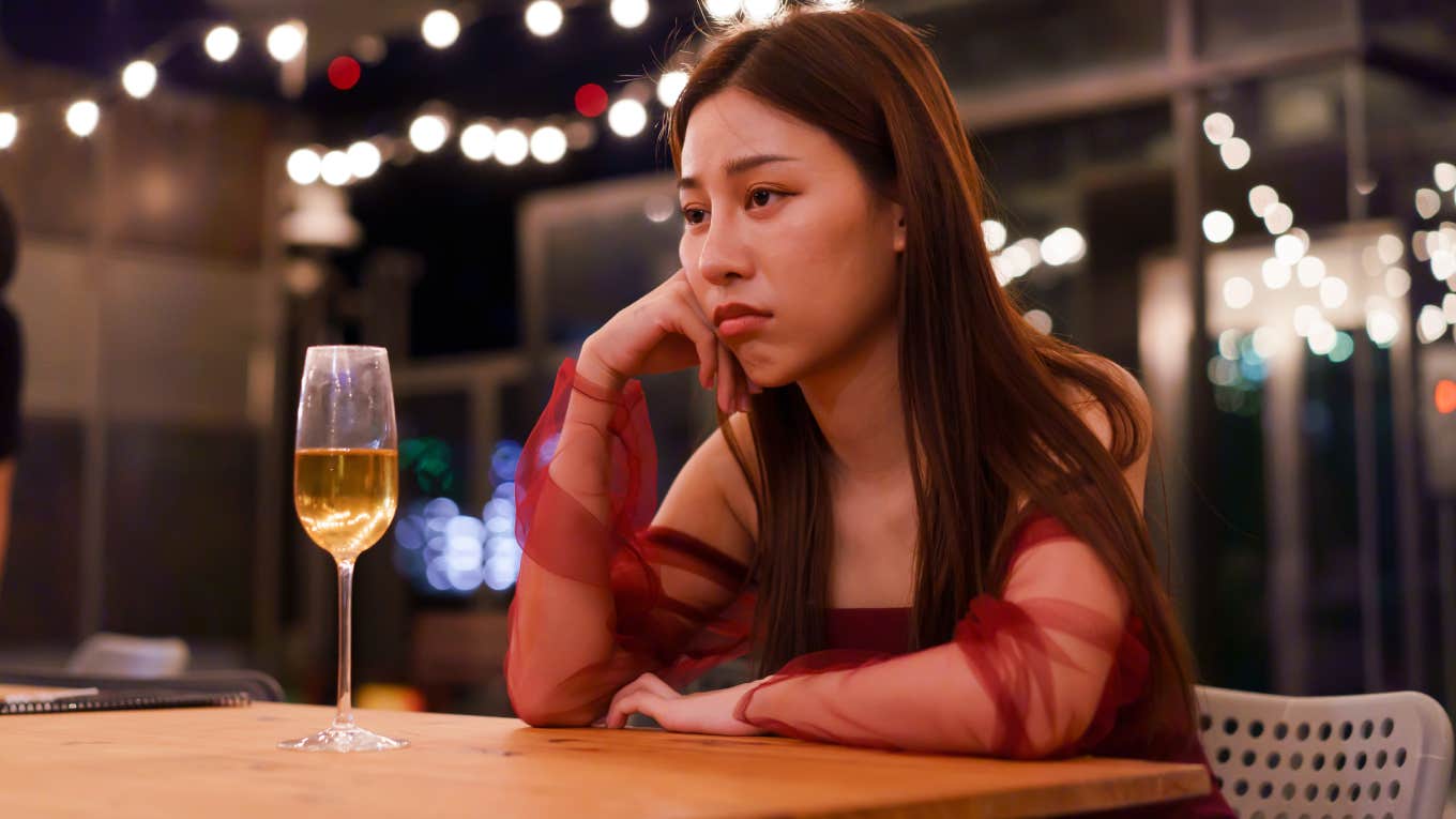 sad woman sitting alone at bar with glass of wine