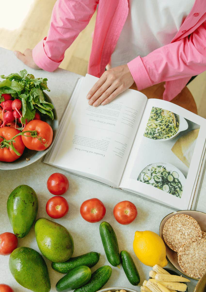 woman turning the page of a cookbook while surrounded by vegetable