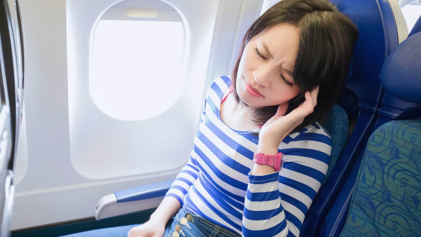 Woman sitting in economy airplane seat looking annoyed. 