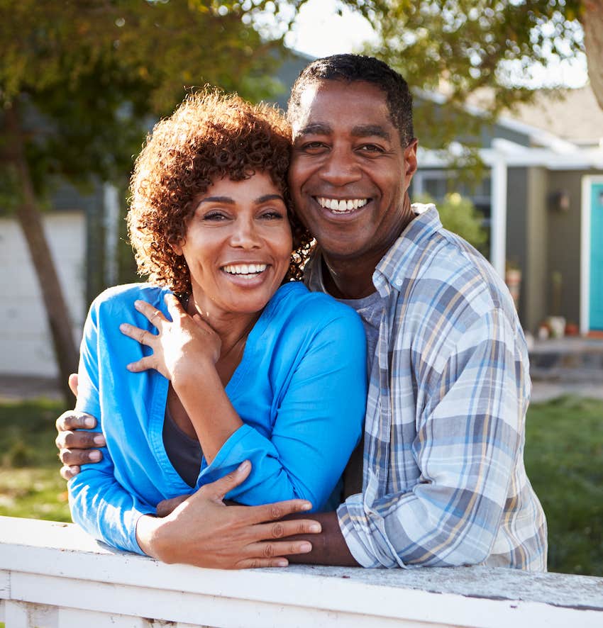 Close couple leans on fence and hugs while smiling