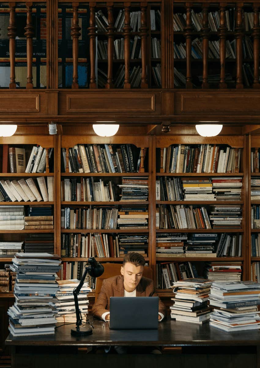 young man on a laptop surrounded by books