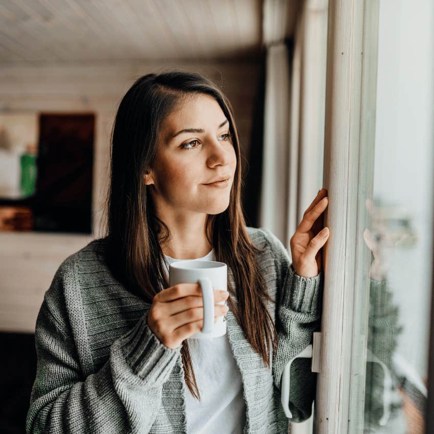 young woman holding mug and looking out of window