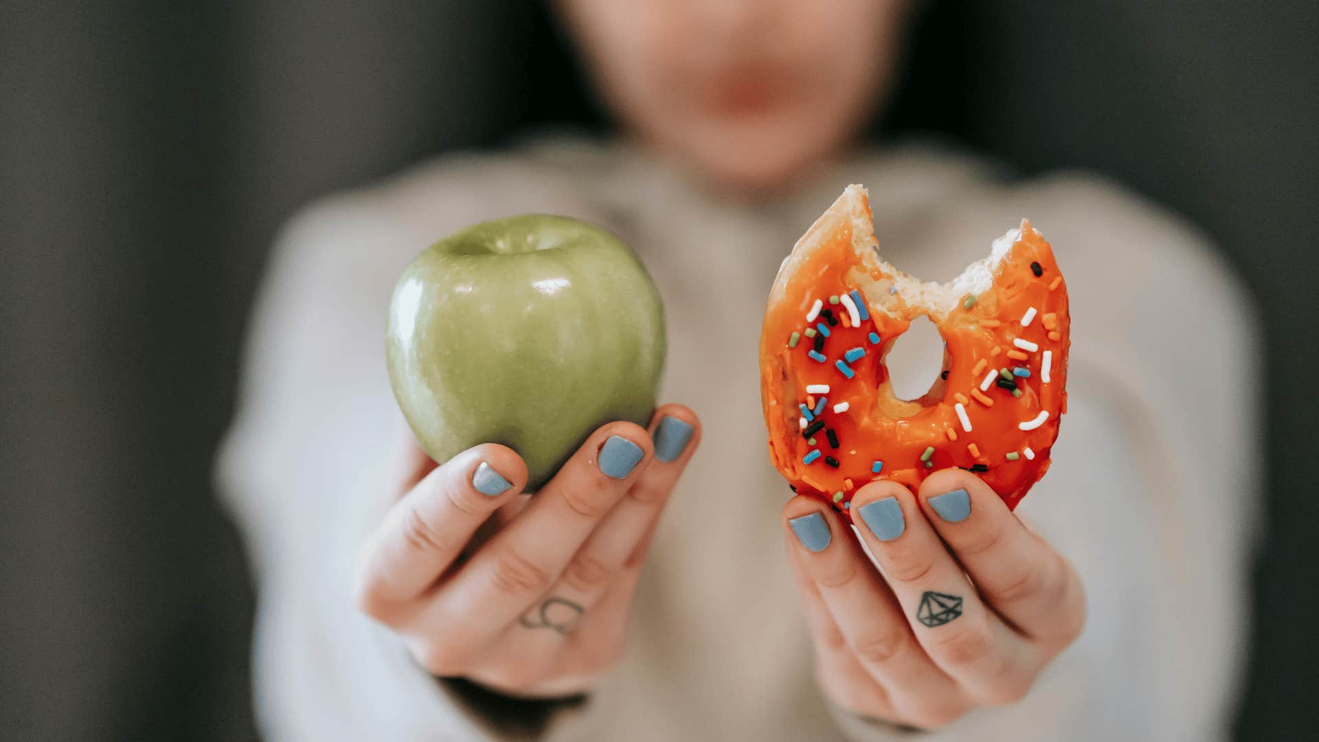 woman holding a green apple and donut in each hand