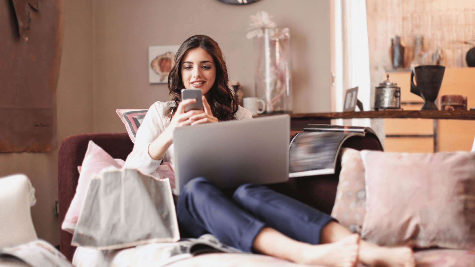 woman with laptop on her lap smiling while texting