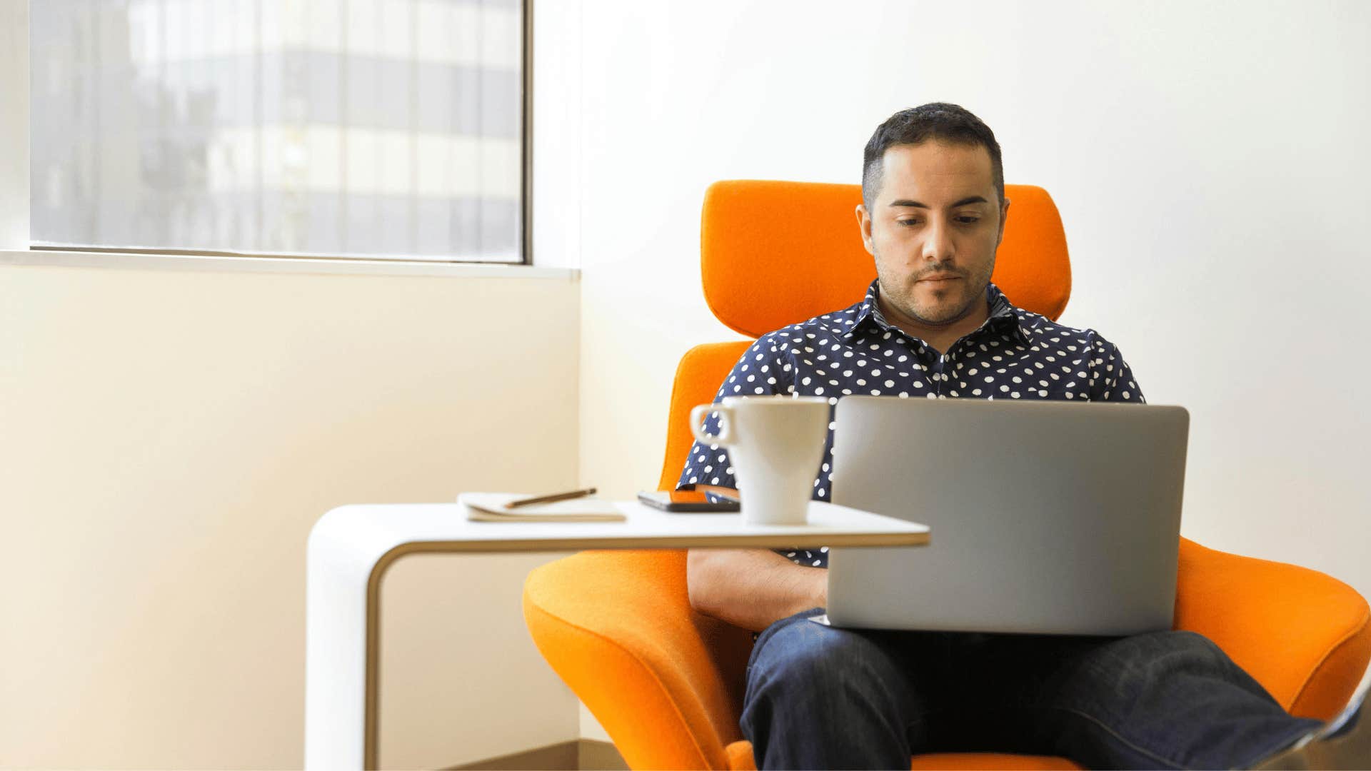 man sitting in an orange chair and working on a laptop