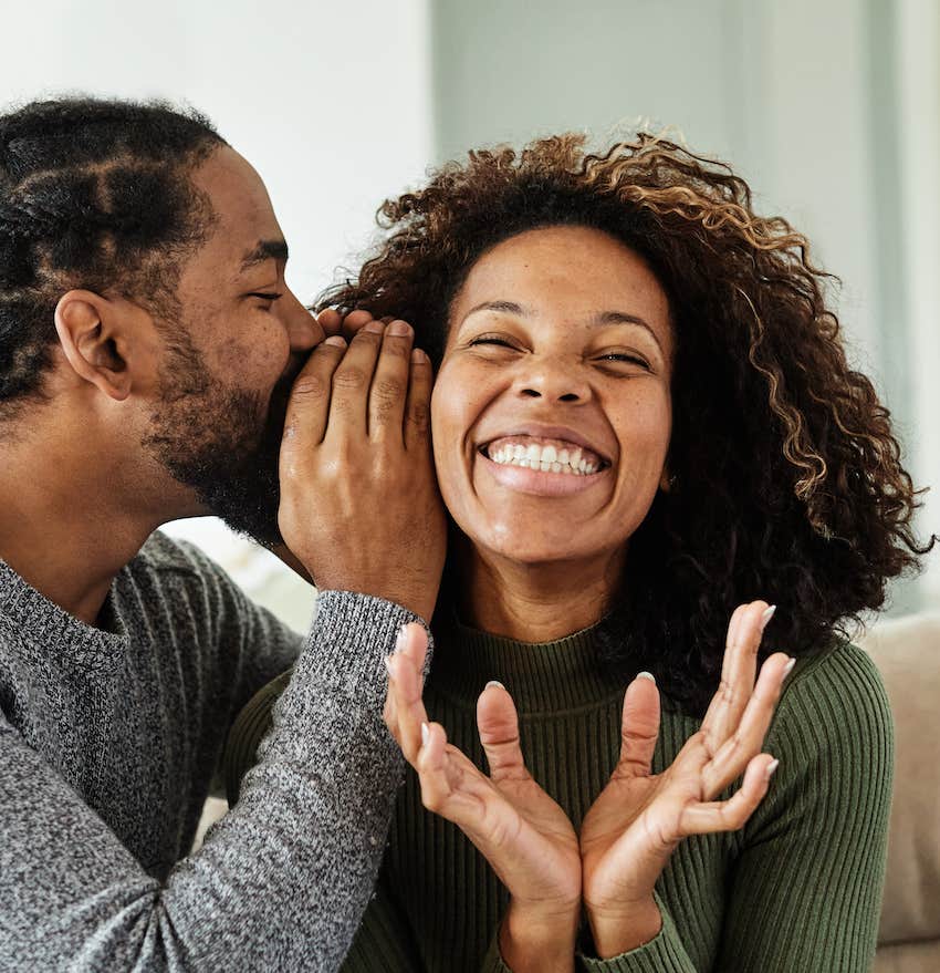 Man whispers a surprise in happy woman's ear