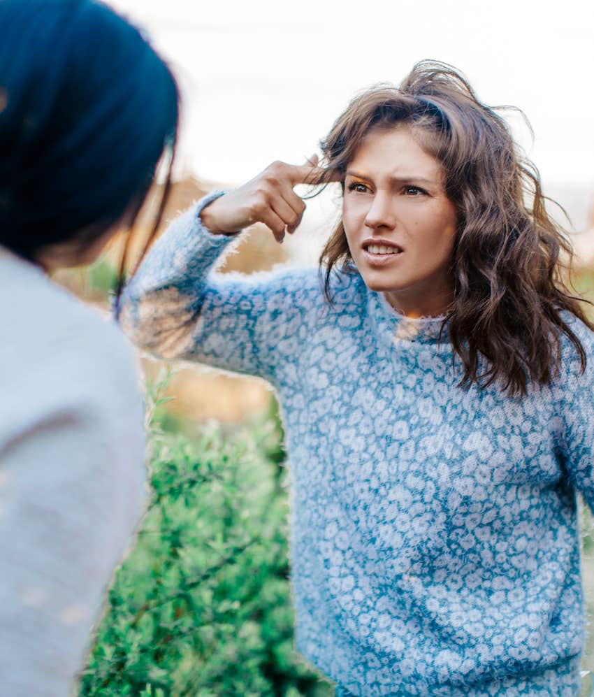 Rude and tired woman points at head while arguing