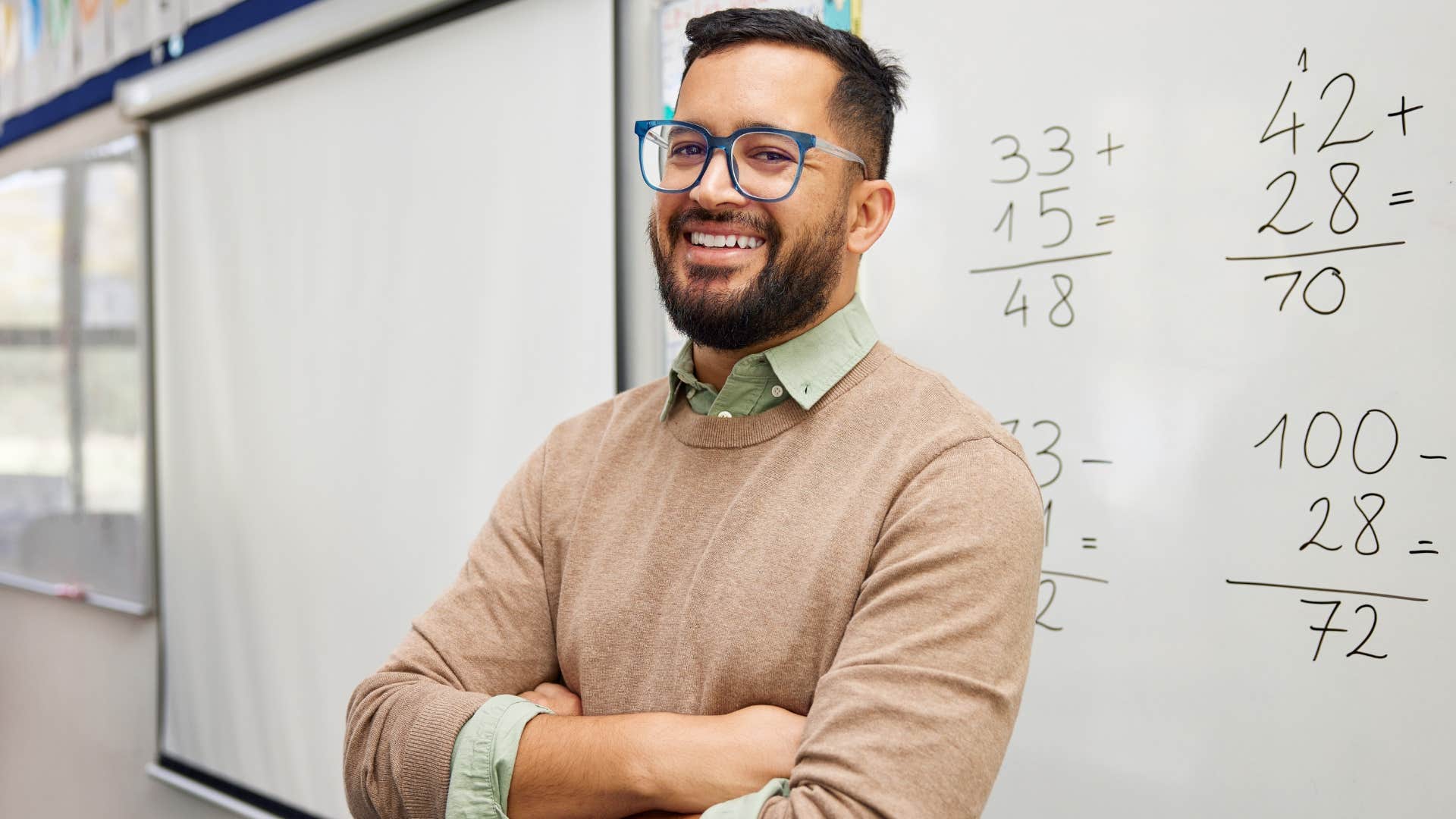 Man smiling with his arms crossed in a classroom.