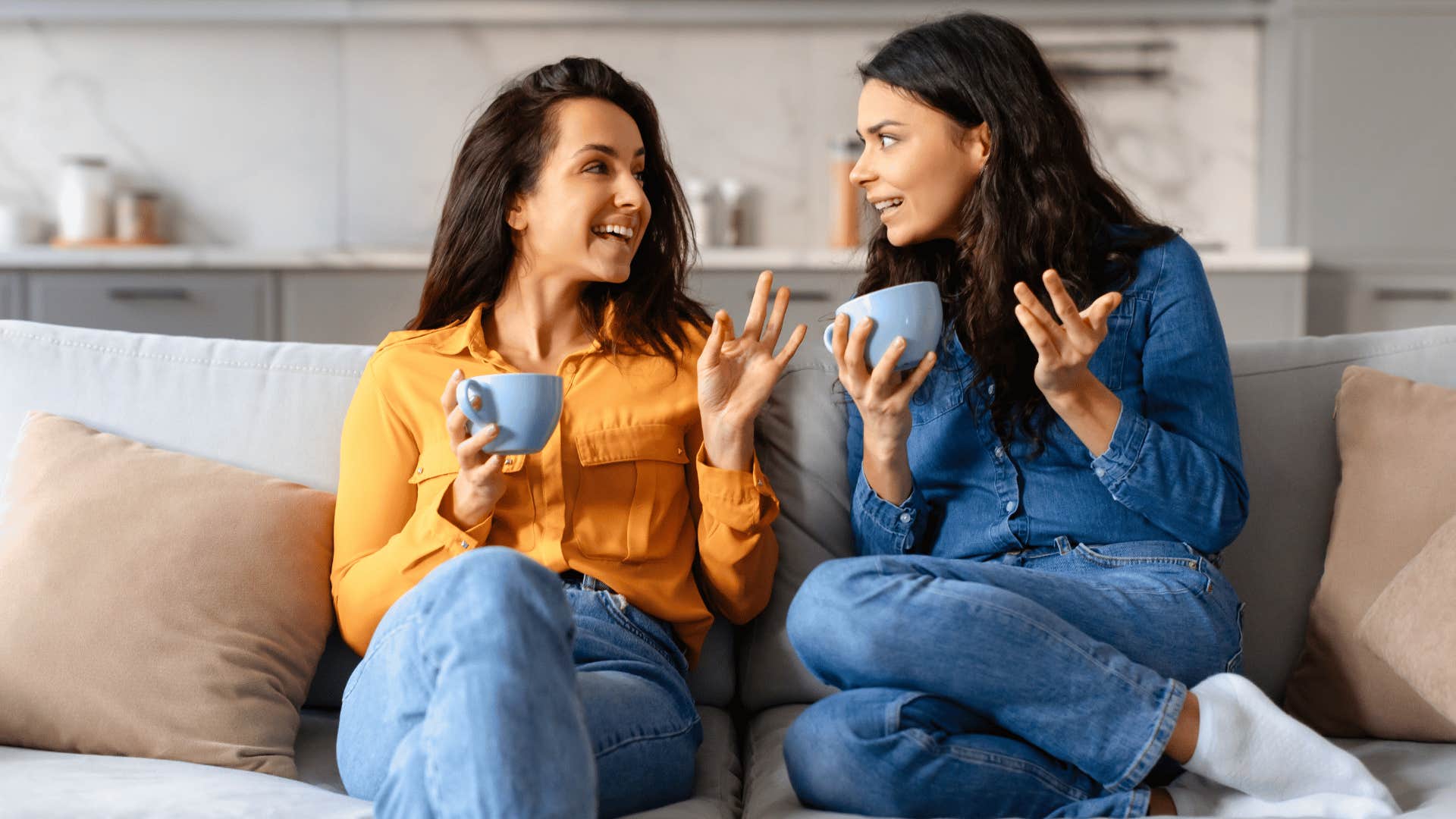 two women talking and drinking coffee on the couch