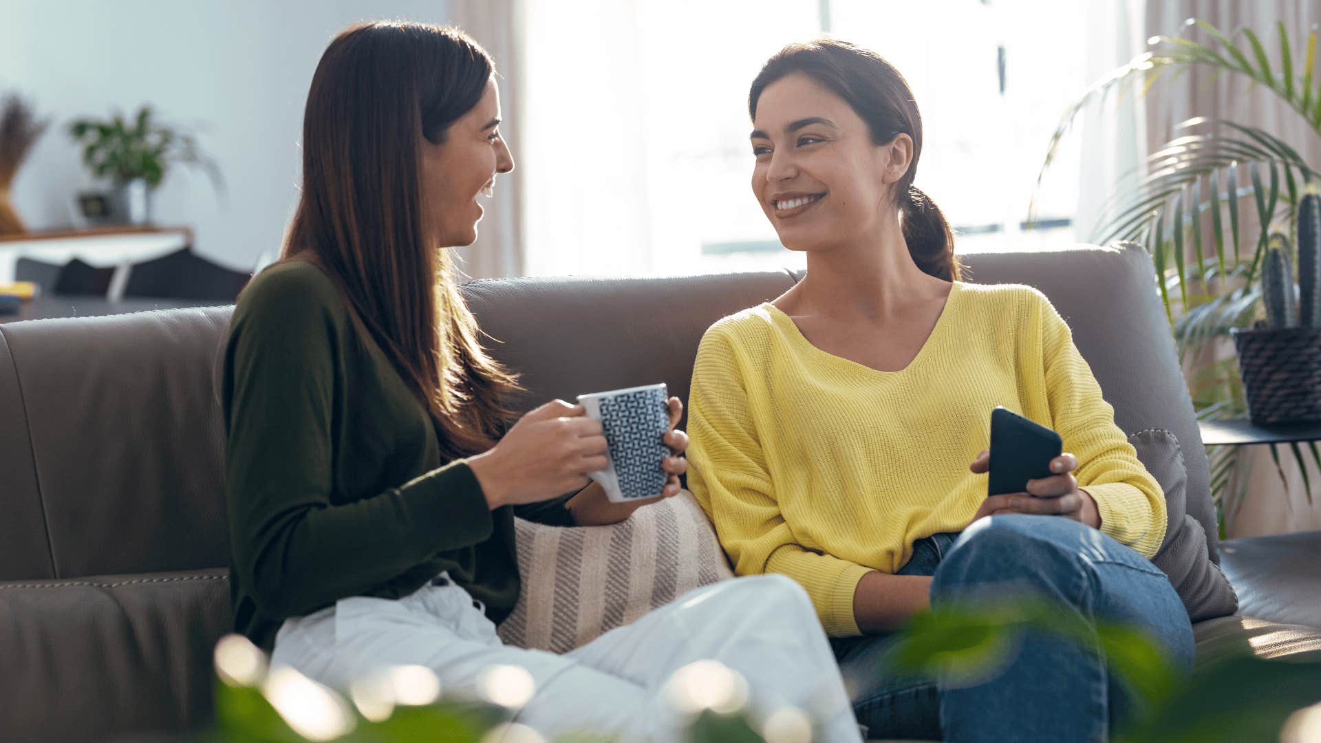 two women chatting on the couch while drinking coffee