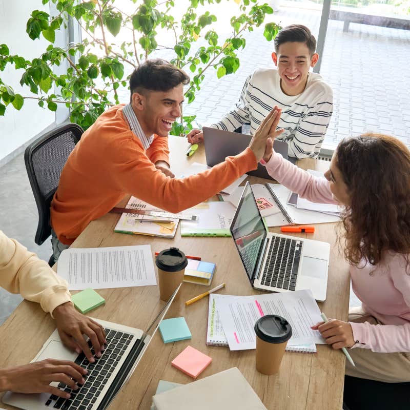 Young happy laughing creative team coworkers celebrate success together giving highfive in office