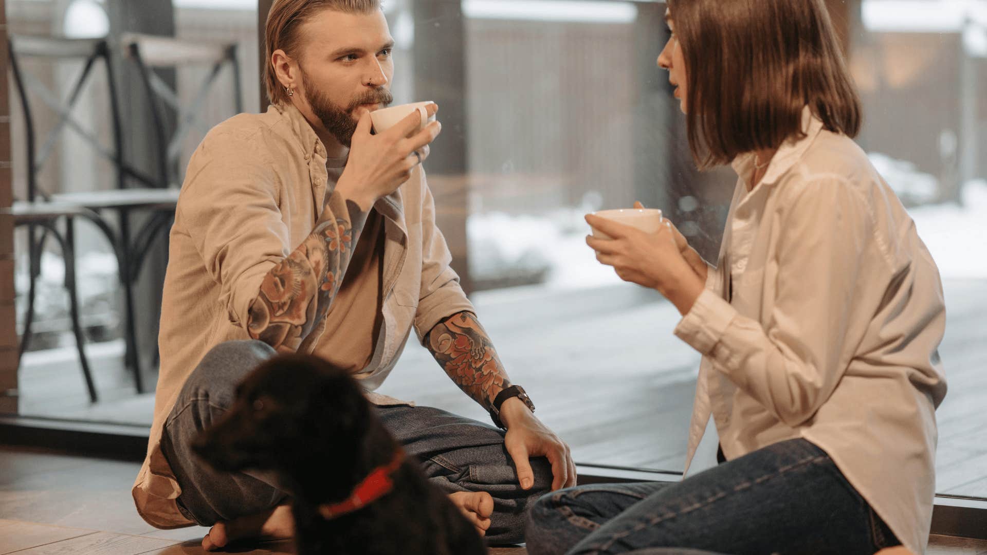 man and woman sitting on ground with hot drinks talking