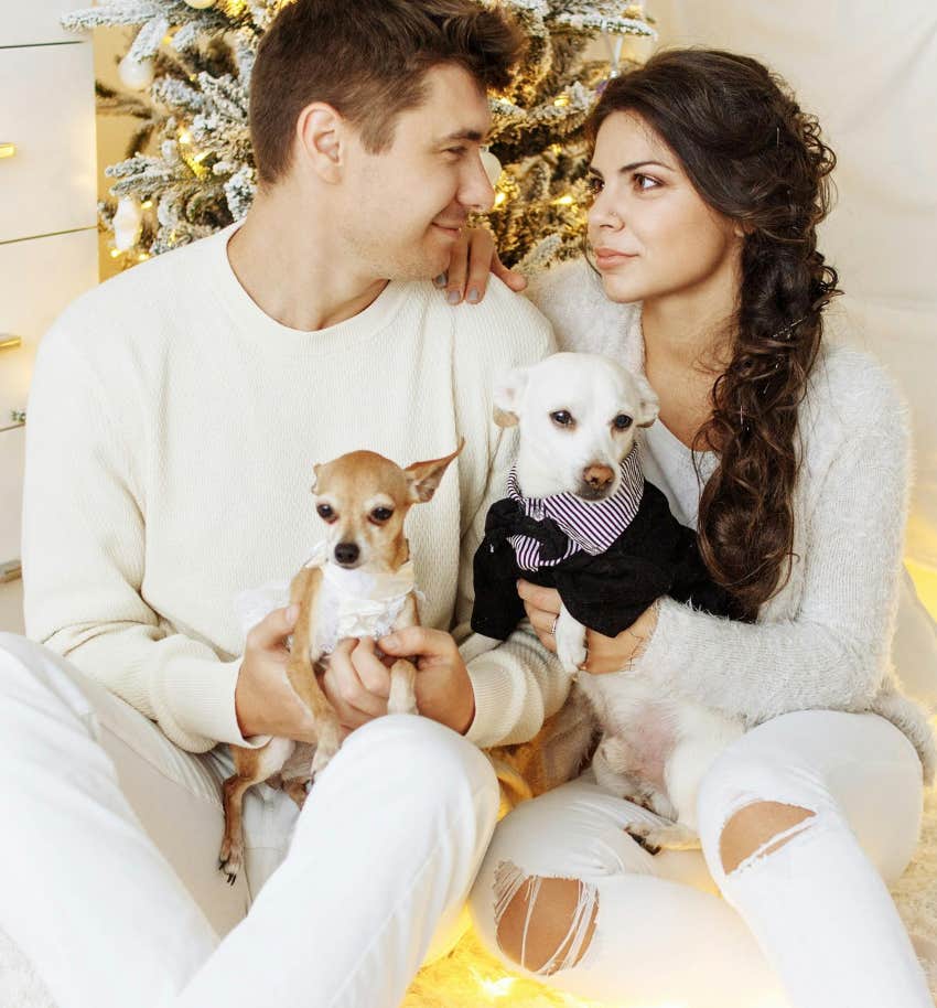 couple sitting in front of Christmas tree holding their dogs