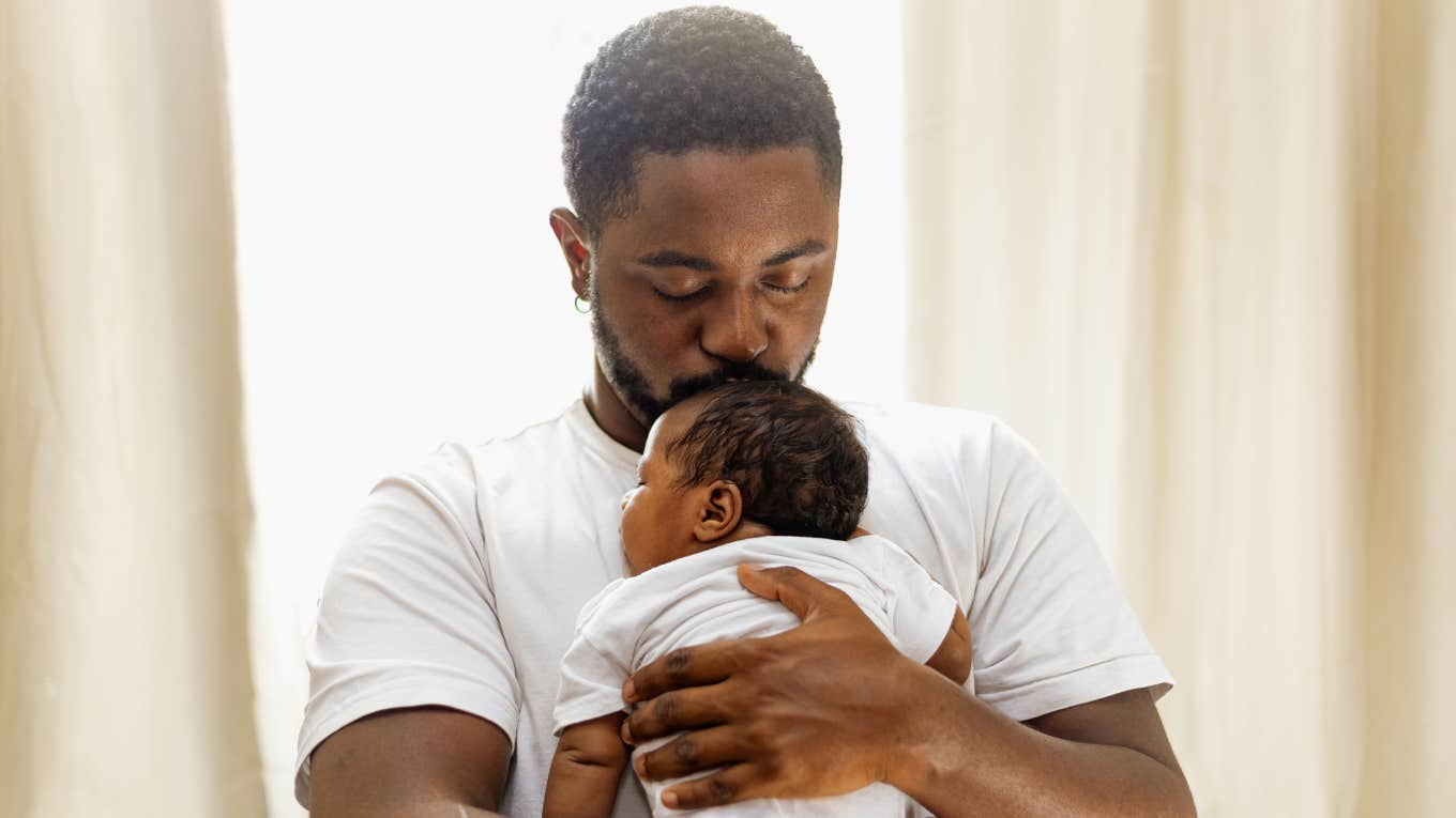 Loving and caring black father giving a hug to his newborn baby daughter at home